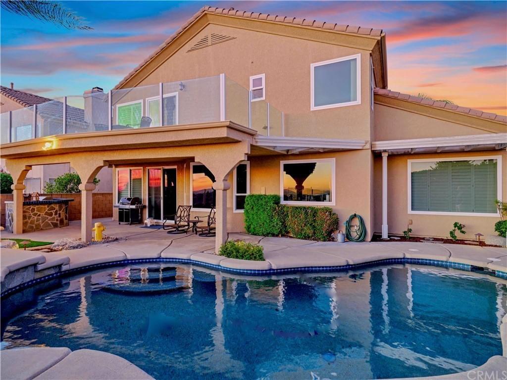 A large home with a second-story deck and covered patio with blue pool in front of a sunset